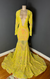 A yellow iridescent sequin v-neck gown with long sleeves and a mermaid train on a mannequin against a dark background by Bellz Couture in Detroit