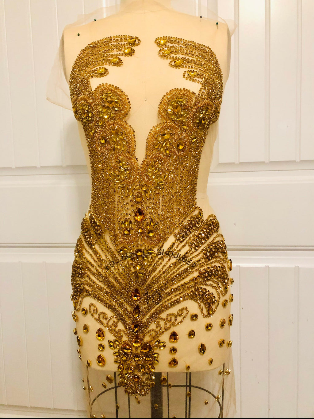 Gold beaded dress on a mannequin against a white paneled wall