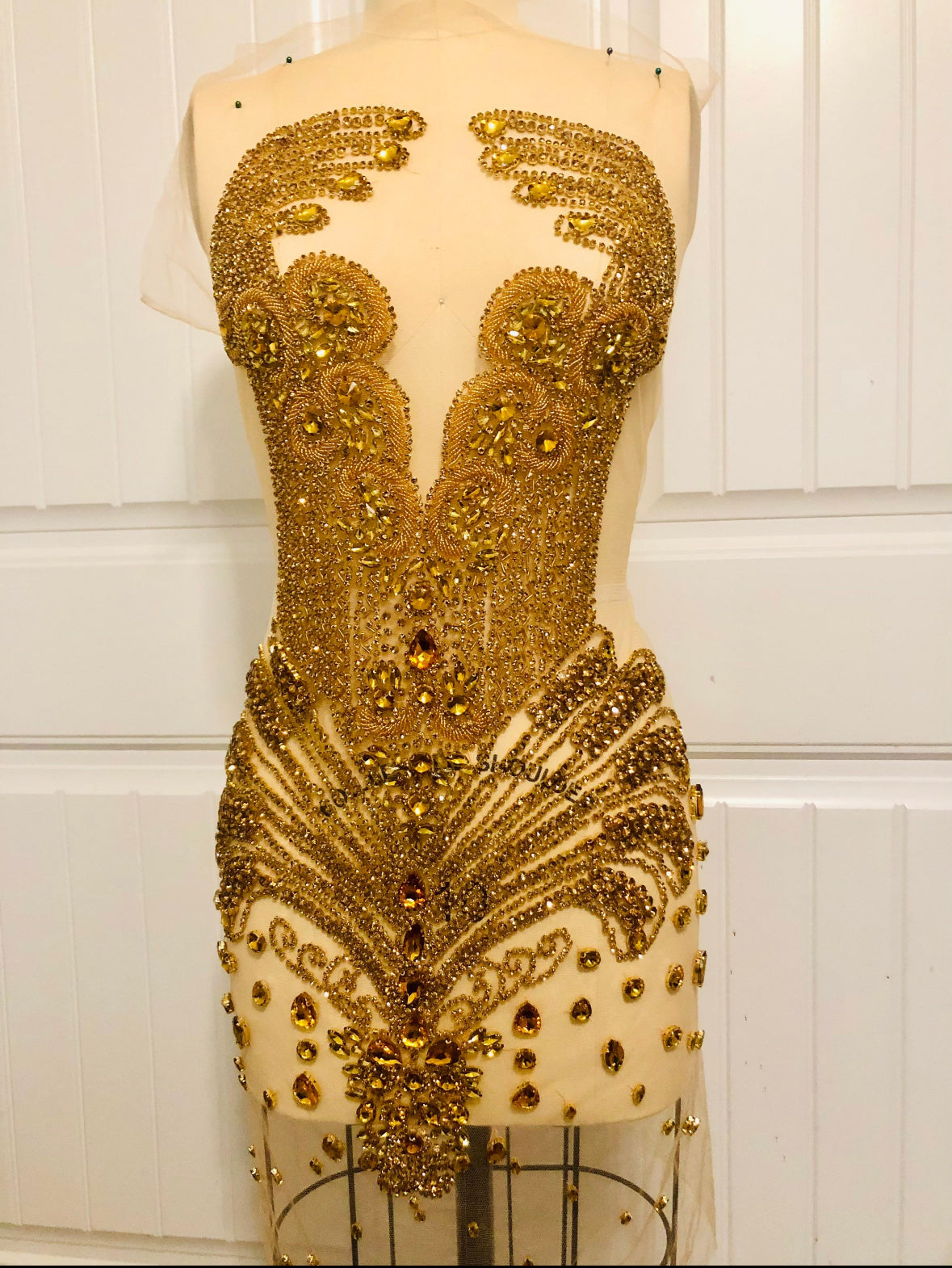 Gold beaded dress on a mannequin against a white paneled wall