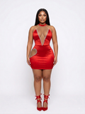 A woman modeling a bright red satin mini dress with a plunging V-neckline trimmed with silver rhinestones, a matching red choker, and red lace-up high heels, set against a plain white studio background.