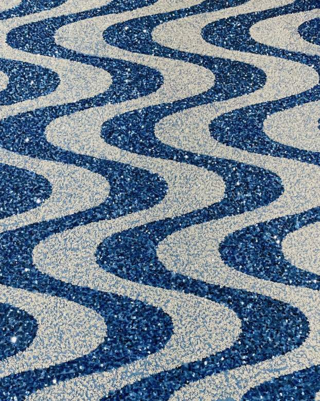 A close-up of a glittery fabric or material with a repeating wavy pattern in deep blue and light silver-gray.